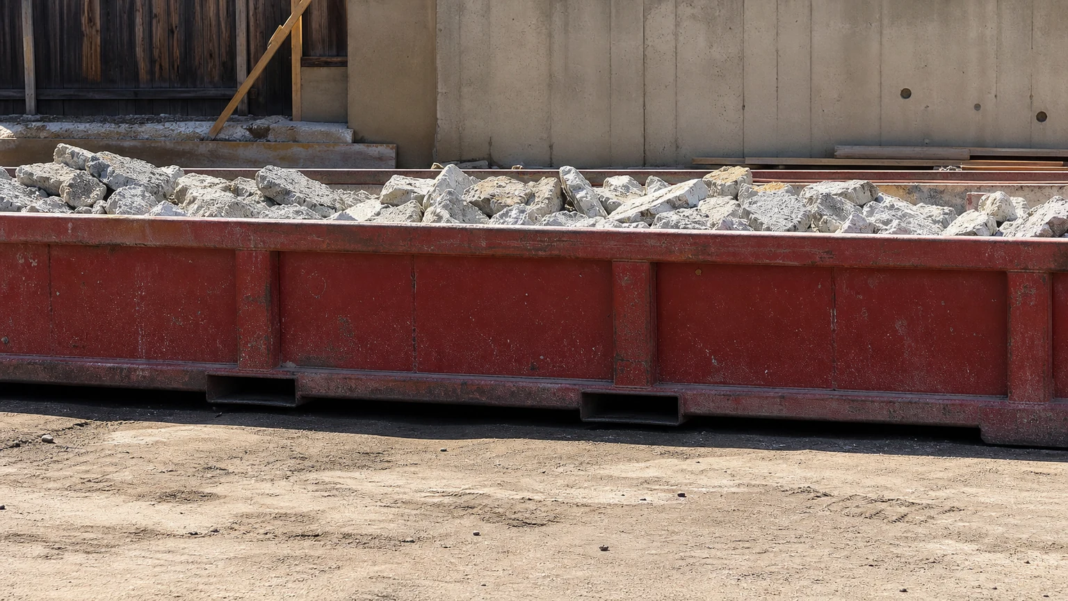 Low red 10 yard lowboy dumpster containing clean broken concrete below the rim