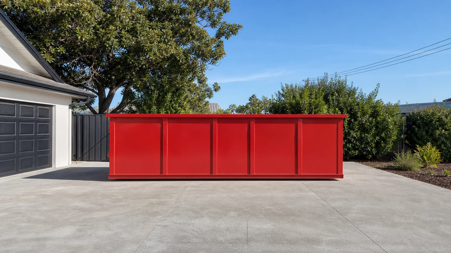 Red roll-off dumpster placed on a wide private driveway with a clear access path