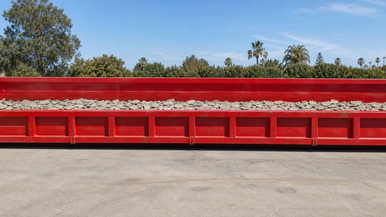 Low-profile red lowboy dumpster containing a shallow clean concrete load below the rim