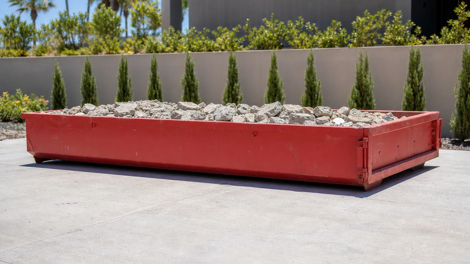Low-profile red dumpster containing a shallow load of clean broken concrete