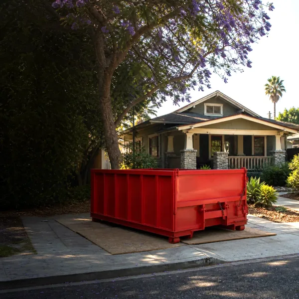 Red roll-off dumpster on protective boards in a residential driveway.