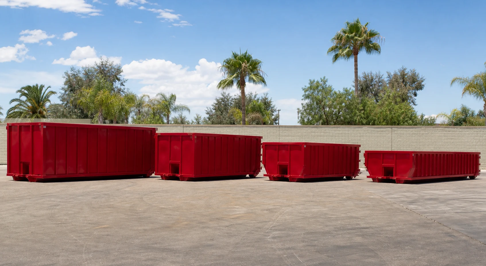 Several clean red roll-off dumpster containers arranged in different sizes on a sunny paved yard