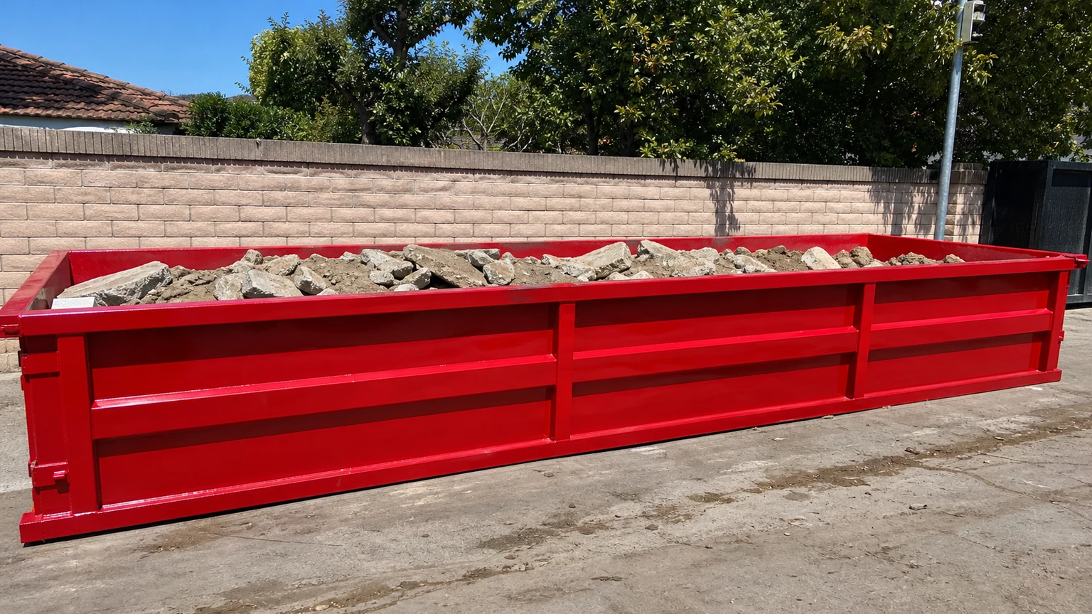 Red low-profile dumpster loaded below the rim with clean concrete for heavy-material disposal