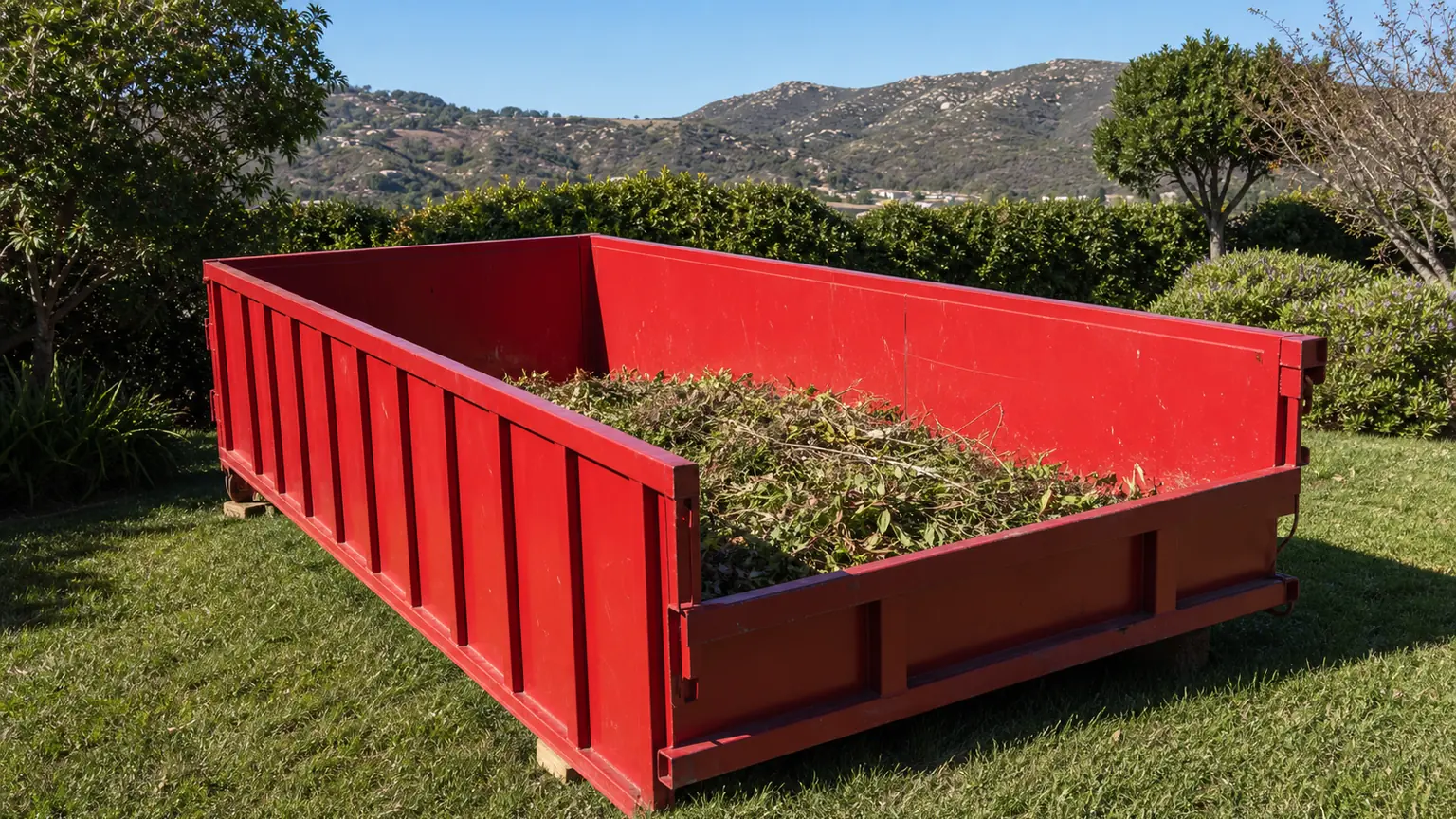 Plain red roll-off dumpster with light yard debris contained below the rim